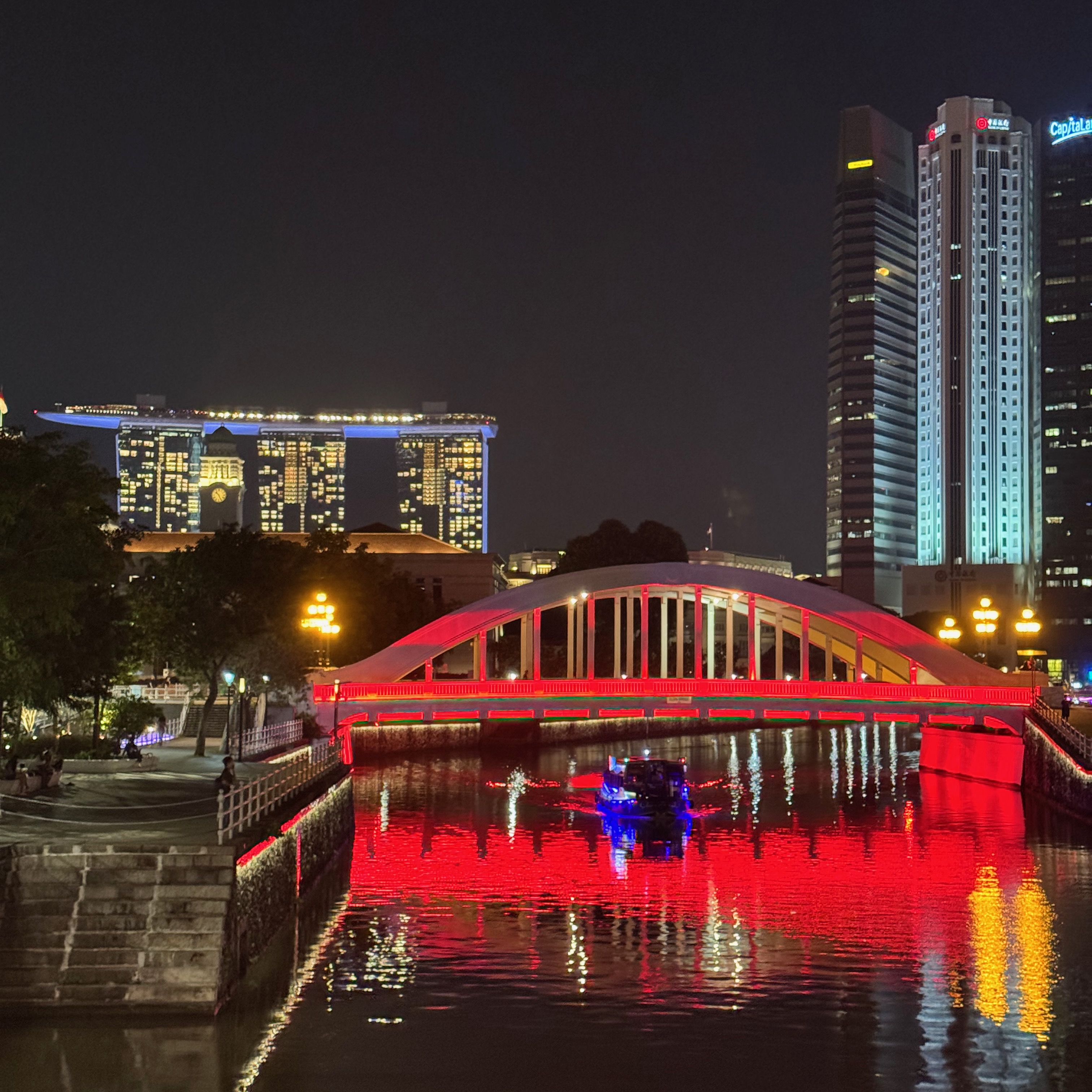 A view of a canal, with a red lit up bridge and the Marina Bay Sands building in the distance
